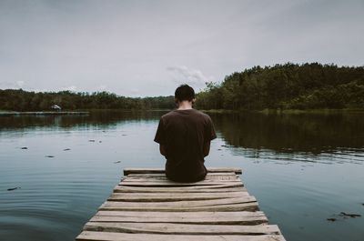 Rear view of man sitting on lake against sky
