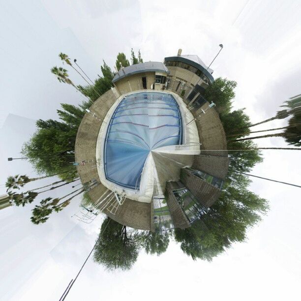 low angle view, tree, architecture, built structure, sky, building exterior, palm tree, day, ferris wheel, outdoors, no people, circle, arts culture and entertainment, amusement park, growth, tall - high, blue, cloud, sunlight, cloud - sky