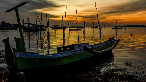 Sailboats moored on sea against sky during sunset