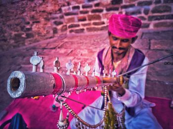 Man in traditional clothing sitting with musical instrument against wall