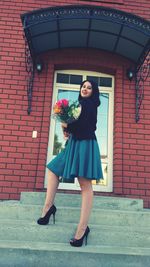 Low angle view of young woman standing against red brick wall