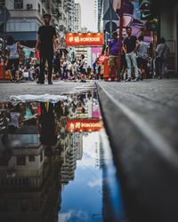 Reflection of people in puddle on street in front of city