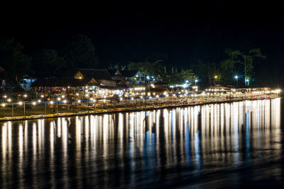 Illuminated buildings by river against sky at night