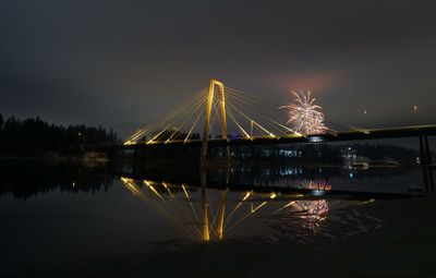 Illuminated bridge over river against sky at night