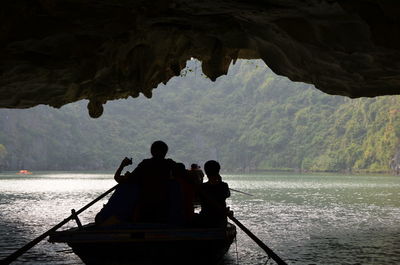 Rear view of silhouette people on boat sailing in sea below cave 