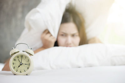 Alarm clock with young woman lying on bed at home