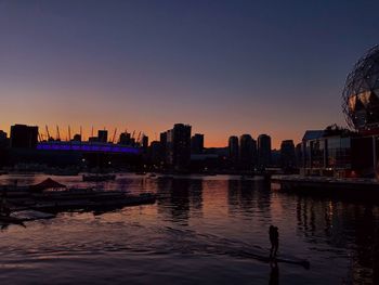 Silhouette buildings by river against sky during sunset