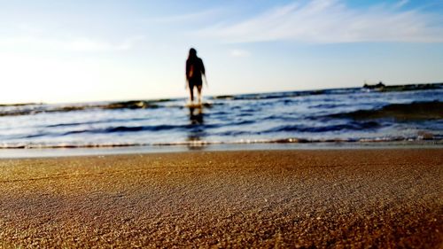 Woman walking on beach against sky during sunset