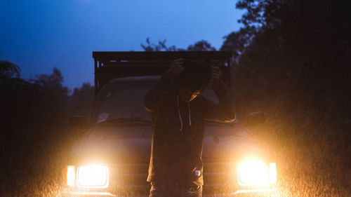 Man standing against illuminated headlight of car