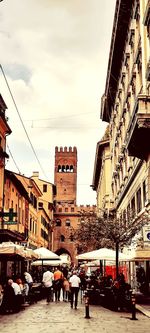 People on street amidst buildings in city against sky