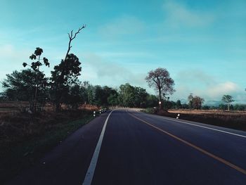 Empty road along trees and against sky