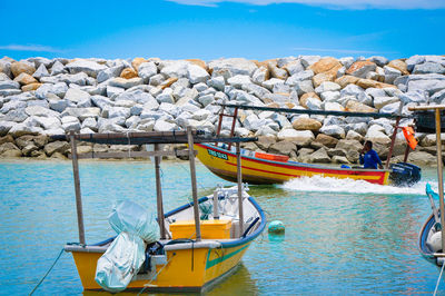 Boats moored on rocks by sea against sky