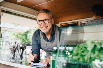 Happy mature owner standing with pen standing in food truck