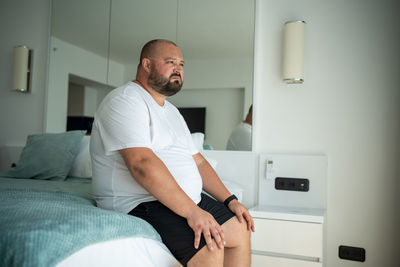 Side view of young man sitting on bed at home