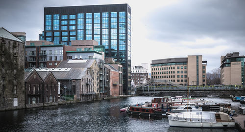 Boats moored in canal amidst buildings in city against sky