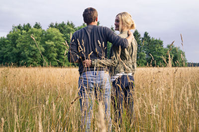 Happy couple standing on grassy field against sky