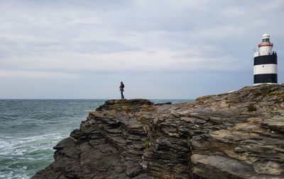 Lighthouse on rock by sea against sky