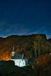 Trees and buildings against sky at night