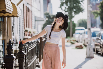 Smiling young woman standing against wall in city