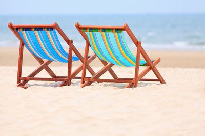 Deck chairs on beach against sky