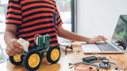 Midsection of boy using laptop while repairing toy on table