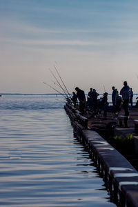 People fishing by sea during sunset