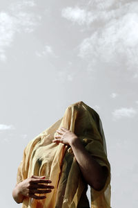 Young woman covered with scarf while standing against sky