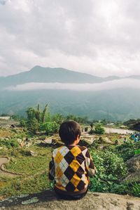Rear view of boy sitting on landscape against sky