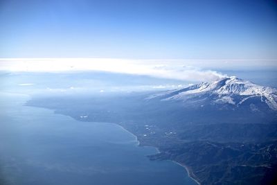 Aerial view of snowcapped mountains and sea against blue sky