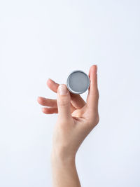 Woman hand holding blank round tin container for lip balm or cream on light gray background