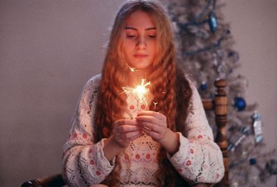 Young woman with burning sparklers by christmas tree at home