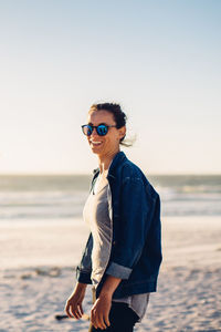 Portrait of smiling young woman standing at beach against sky