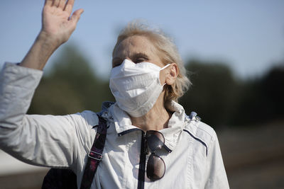 Happy elderly senior old woman with medical face mask and raised hand for greeting