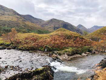 Scenic view of stream by mountains against sky