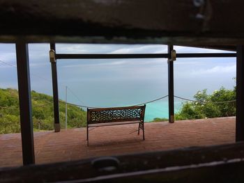 Empty benches against sky seen through window