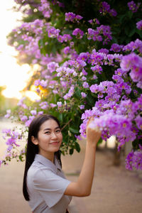 Portrait of smiling woman standing against purple flowering plants