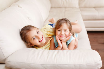 Two cute little caucasian girls siblings playing at home. adorable children kids lying on couch