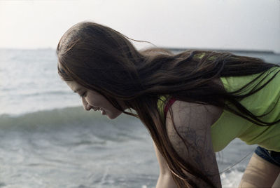 Side view of young woman bending by sea