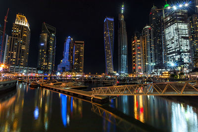 Illuminated cityscape by sea against sky at night