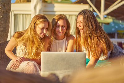 Happy woman with friends using laptop on sunny day