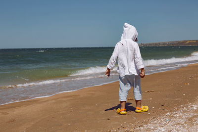 Baby boy walk on the beach with sand in yellow slippers and white shirt