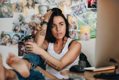 Thoughtful woman with coffee cup sitting on chair against wall