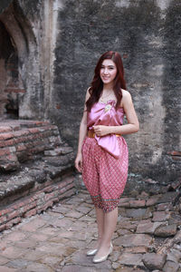 Portrait of a beautiful young woman standing against pink background