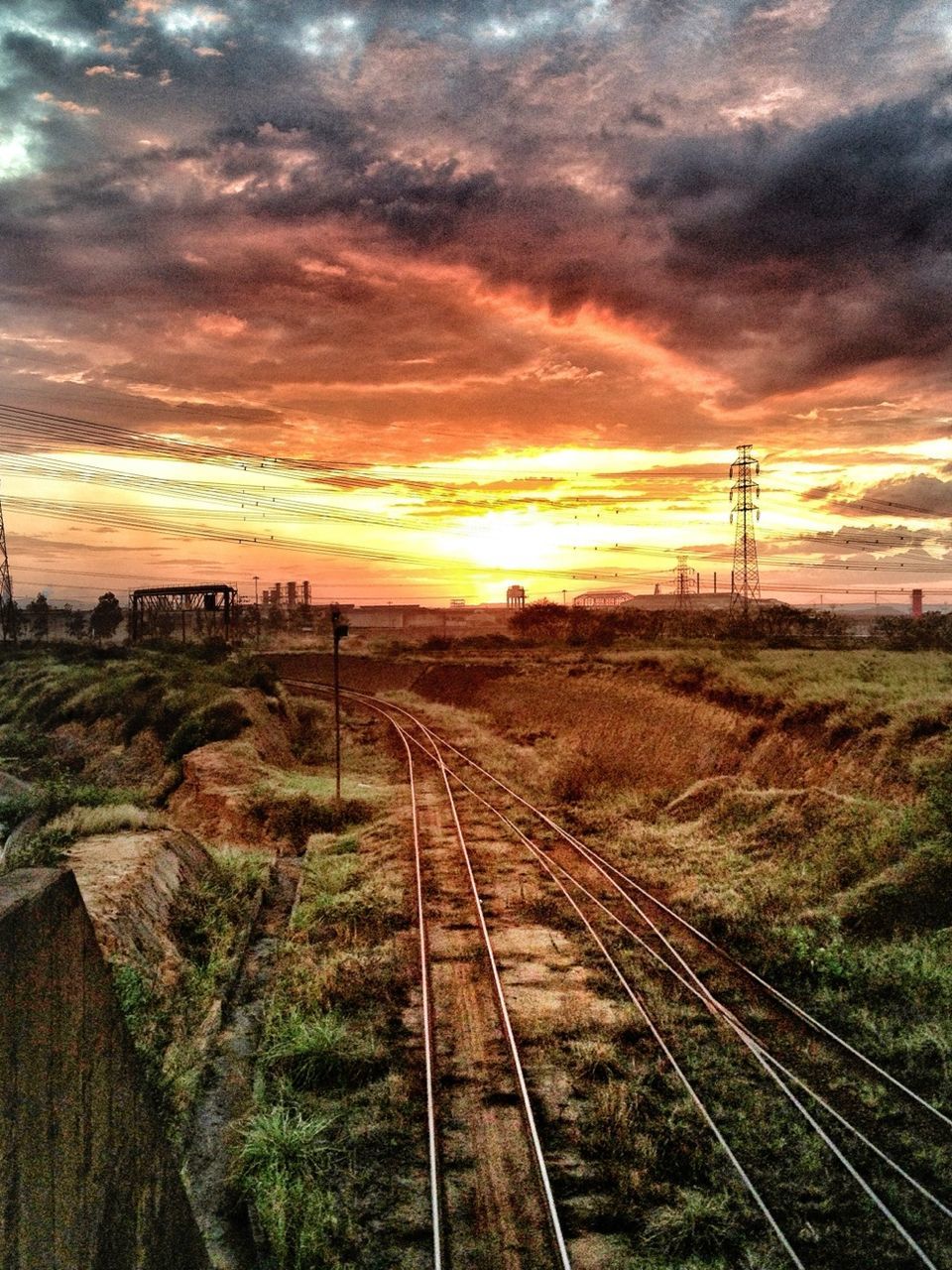 railroad track, sunset, rail transportation, sky, transportation, cloud - sky, landscape, the way forward, orange color, diminishing perspective, vanishing point, tranquil scene, nature, power line, electricity pylon, cloudy, field, tranquility, beauty in nature, cloud