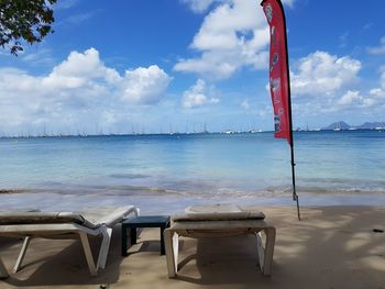 Deck chairs by sea against sky