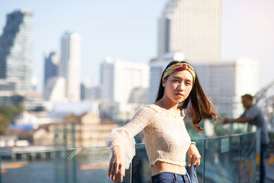 Portrait of young woman standing against railing in city