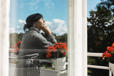 Smiling woman enjoying sunlight in balcony seen through glass