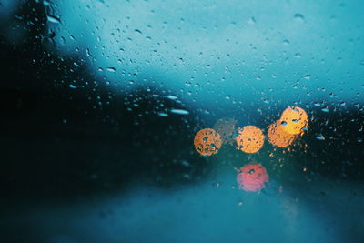 Illuminated lights seen through wet glass window on rainy day