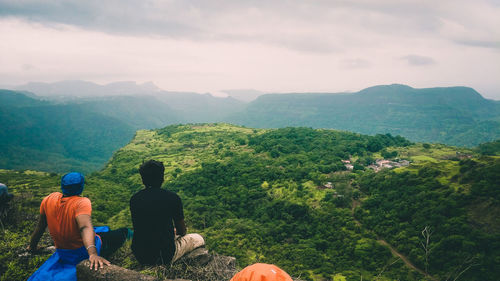 Rear view of men sitting on mountain against sky enjoying the view