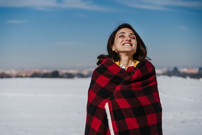 Smiling young woman standing in snow against sky